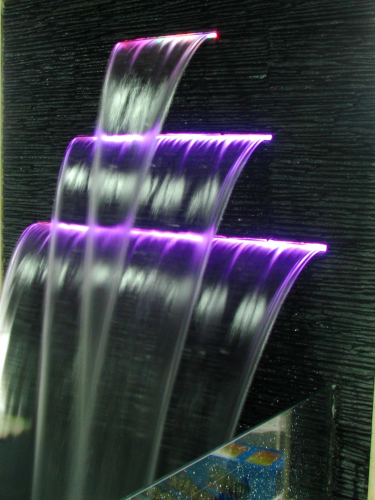 Example effect of Emaux Water Descent equipment: a row of 3 cascading waterfalls with strips of LED light embedded in openings to give colour to the waterfall (purple in photo).